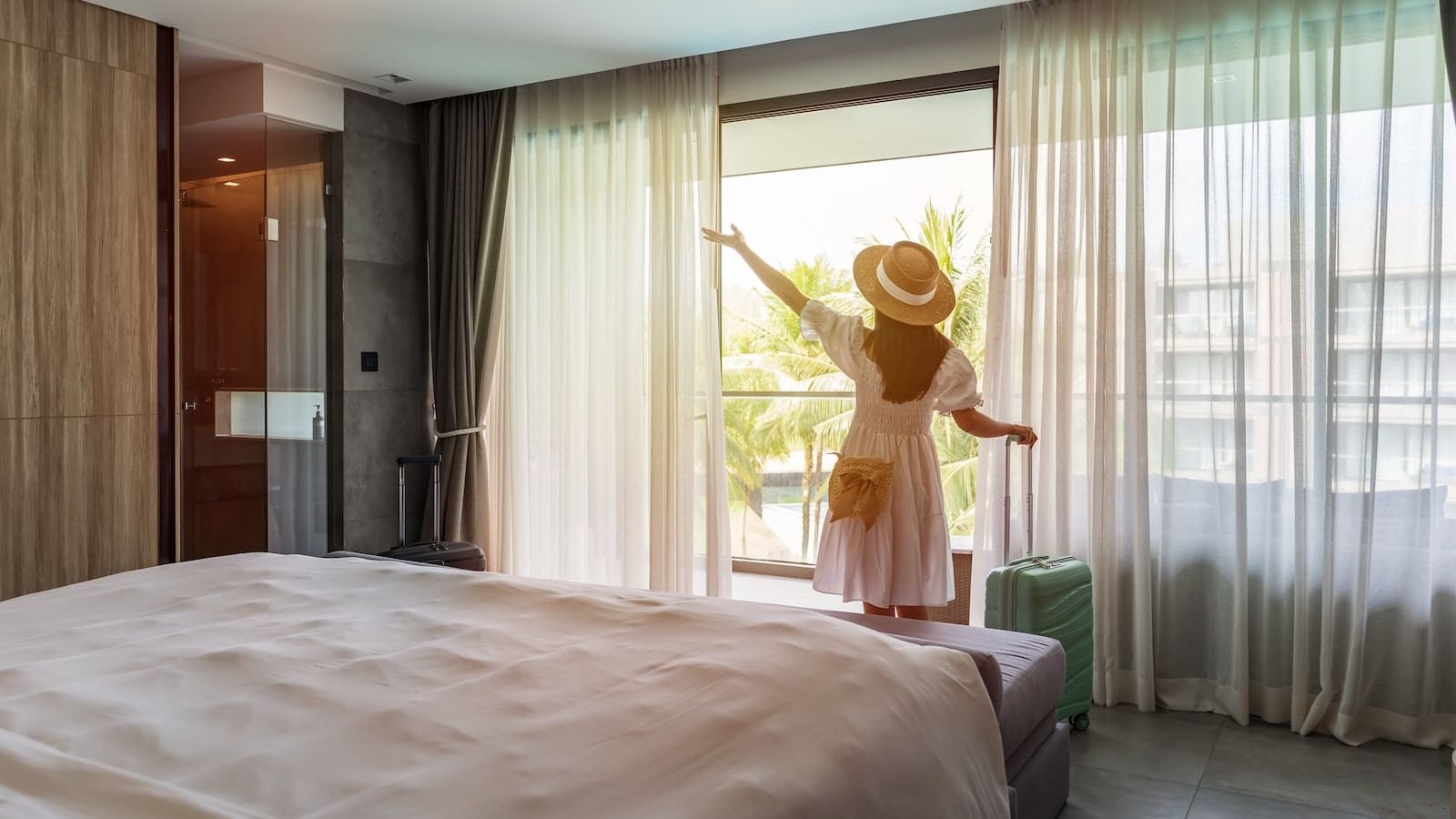 Traveler standing in a hotel room with luggage beside a large window