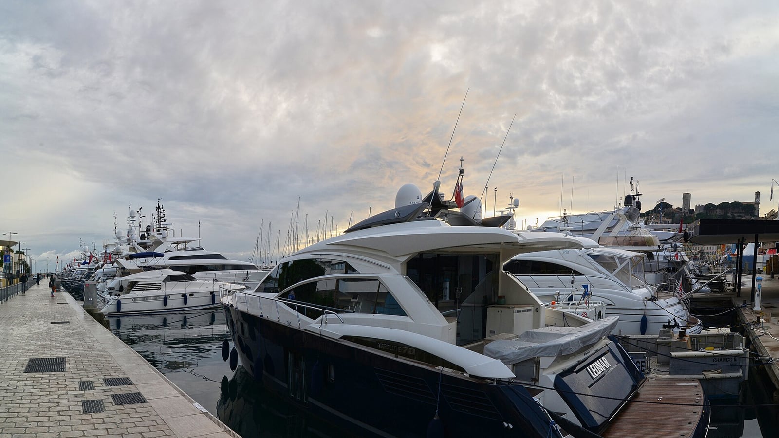 A sunny view of Le Vieux Port in Cannes, France, with luxury yachts and small boats moored in front of historic buildings.