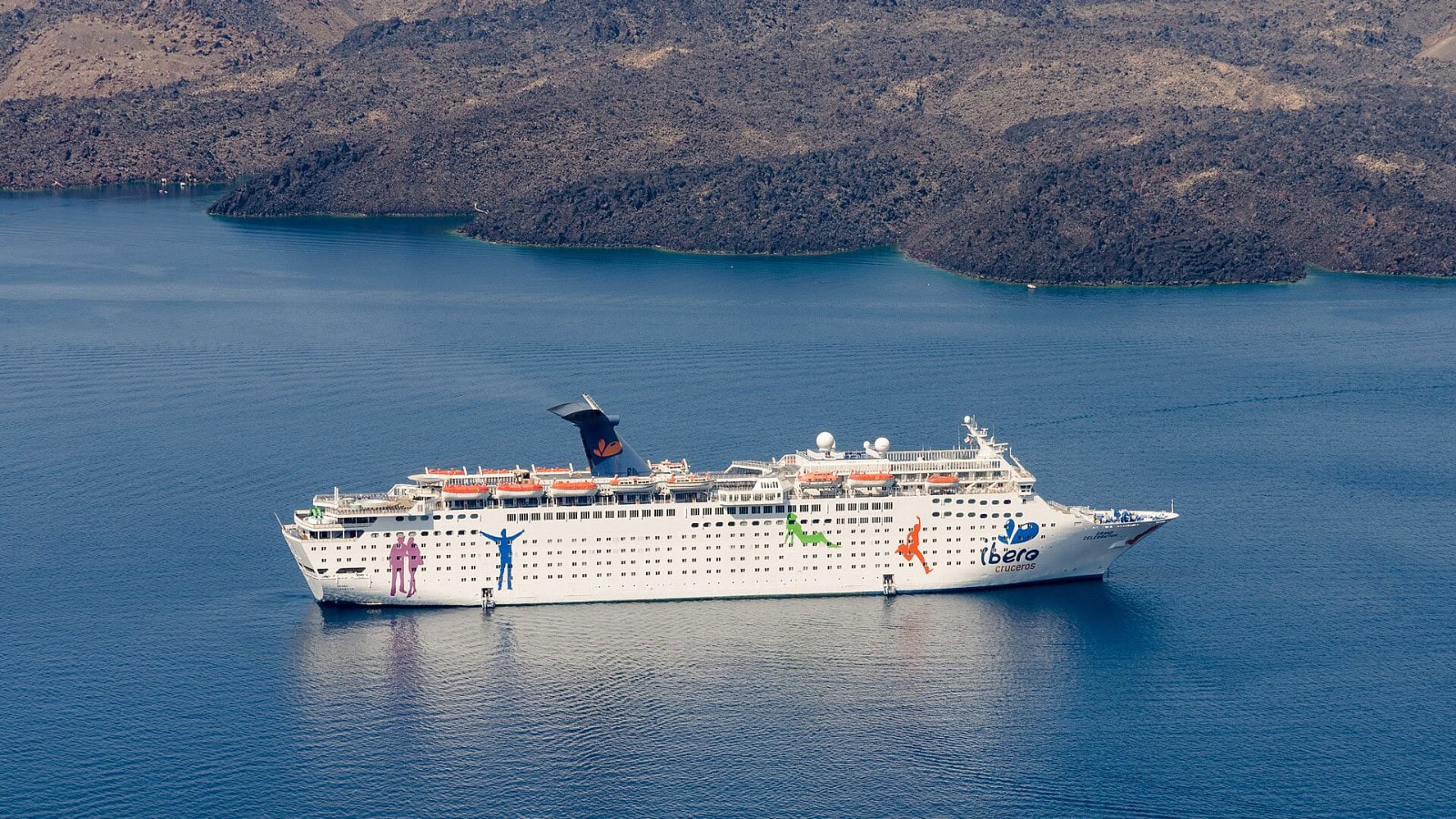 The cruise ship Grand Celebration anchored off Santorini, Greece, with the island caldera cliffs behind it