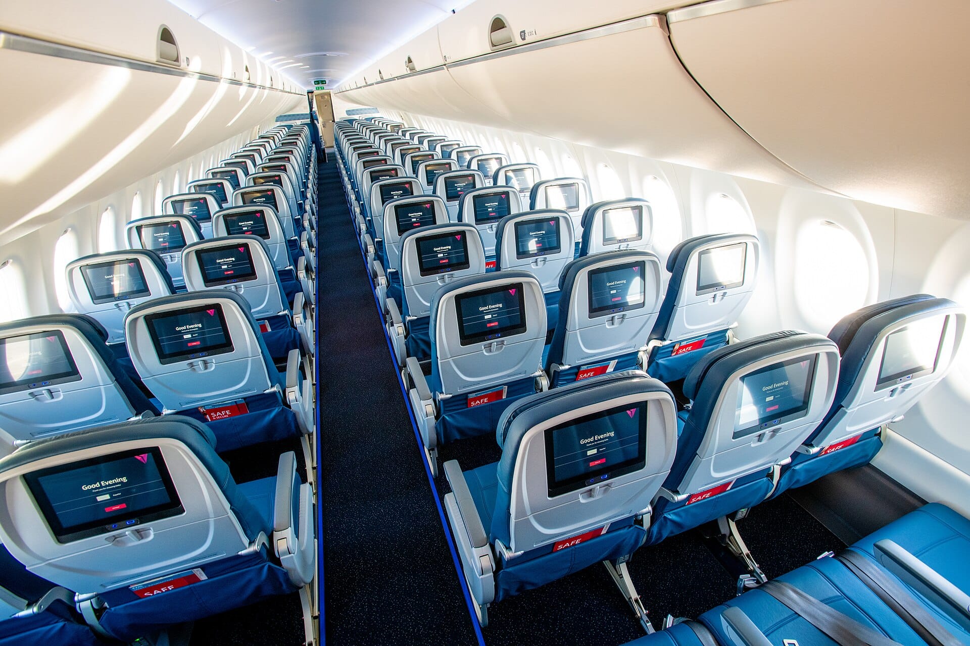 An airplane economy cabin interior, where the personal item goes under the seat in front of you