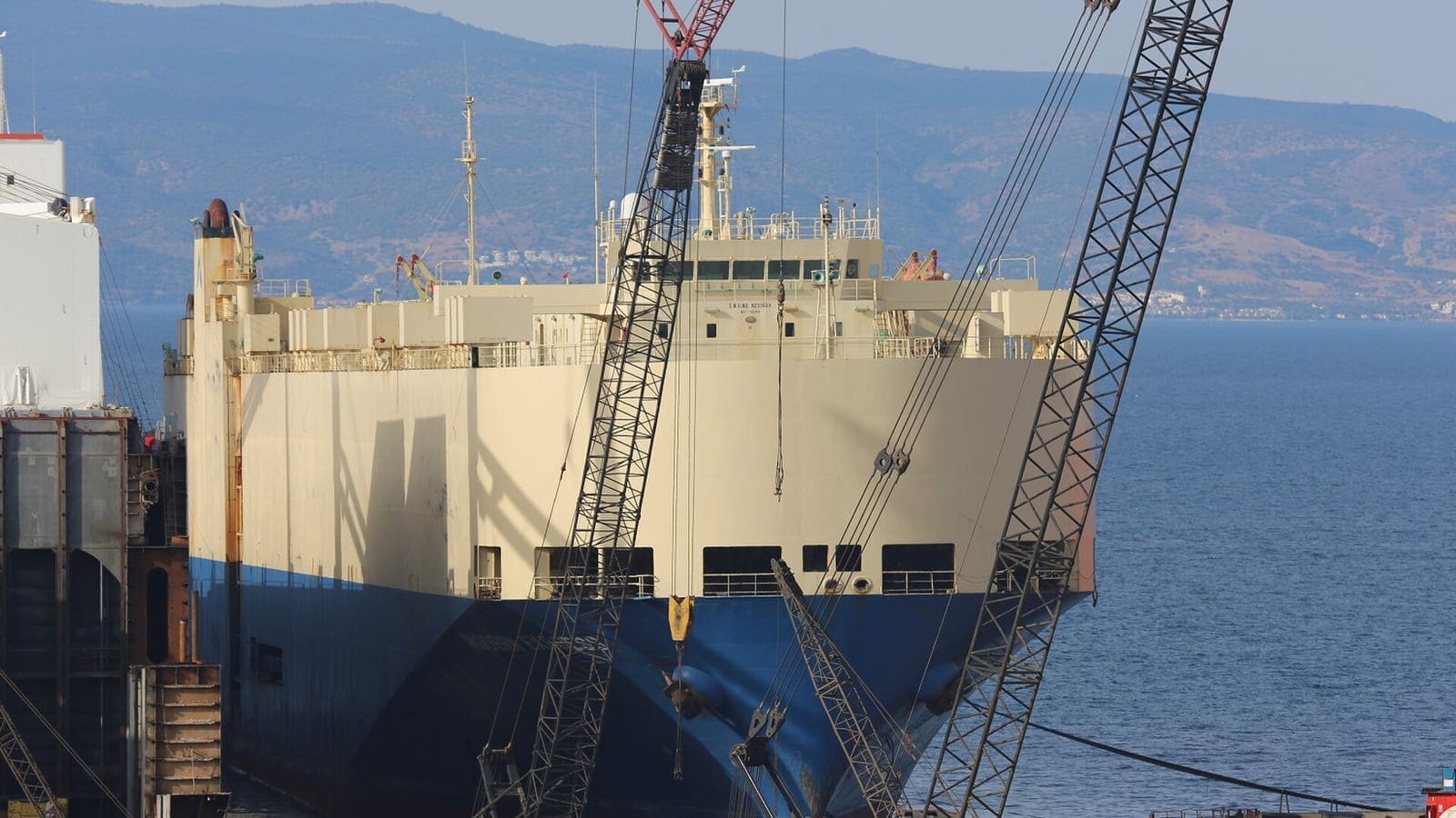 A massive heavy-lift crawler crane dismantling a large ship beached on the shoreline at Aliağa.