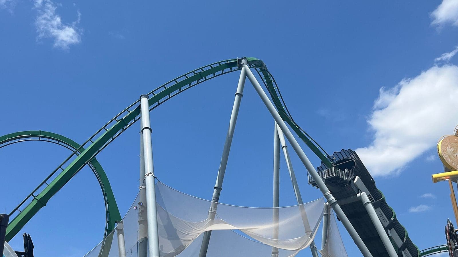 A wide daylight photograph of the roaring, bright green steel track of the Incredible Hulk Coaster looping over the water at Universal's Islands of Adventure.