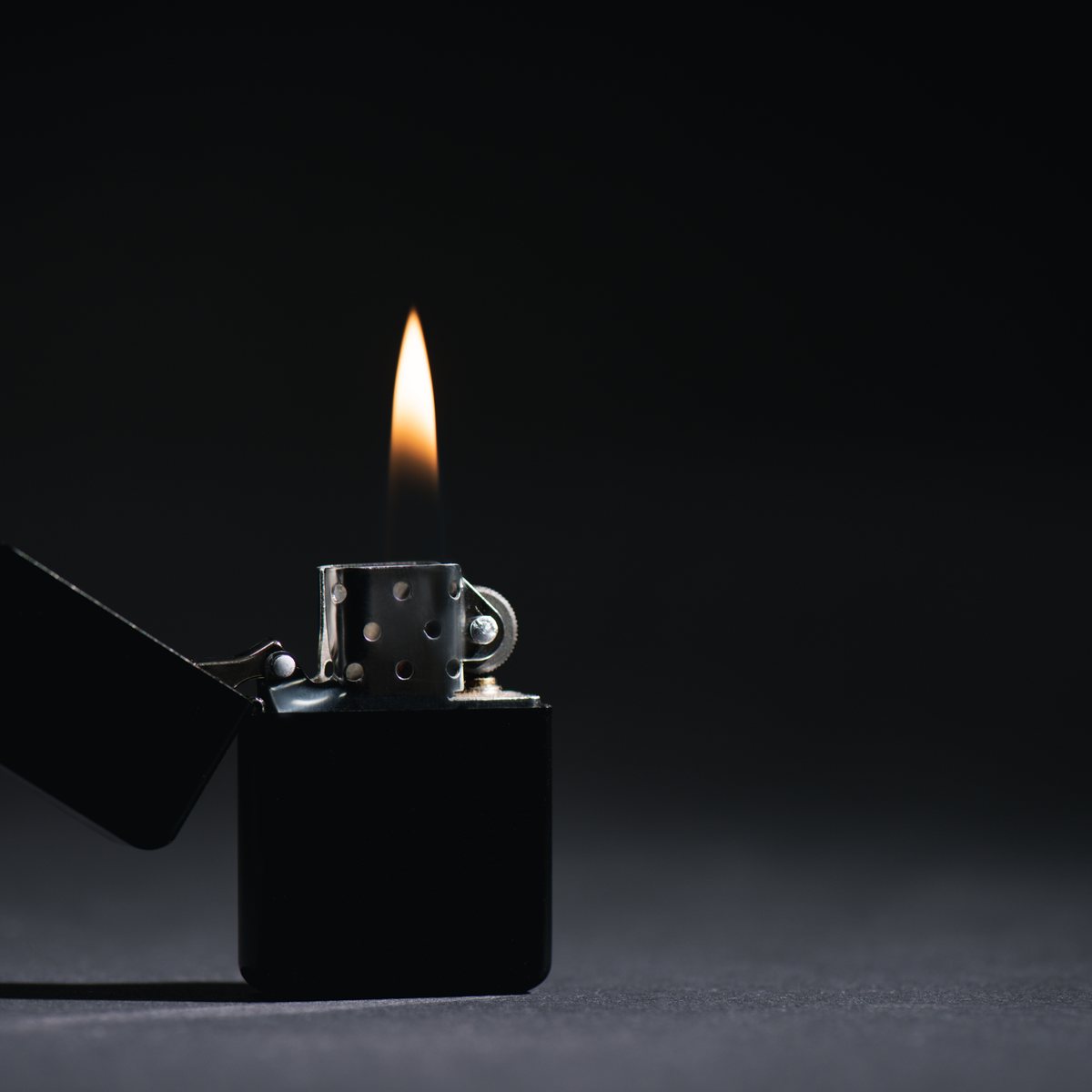 Black Zippo style lighter with open flame on a dark background
