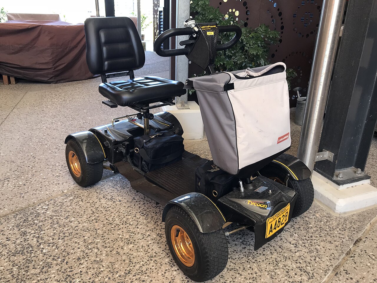 A modern, bright red folding travel mobility scooter parked on a paved walkway on a sunny day.