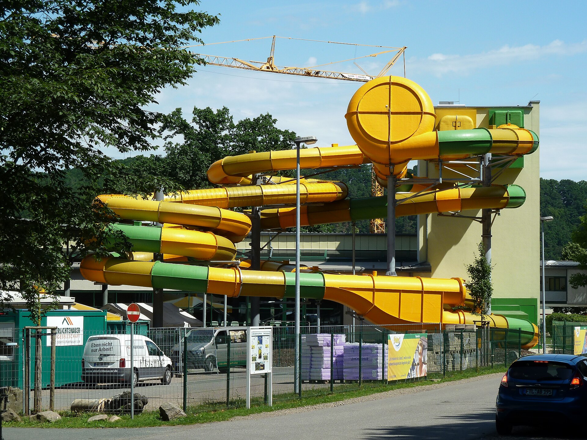 A modern curved water slide structure where two riders can ride tire tubes under bright blue skies.