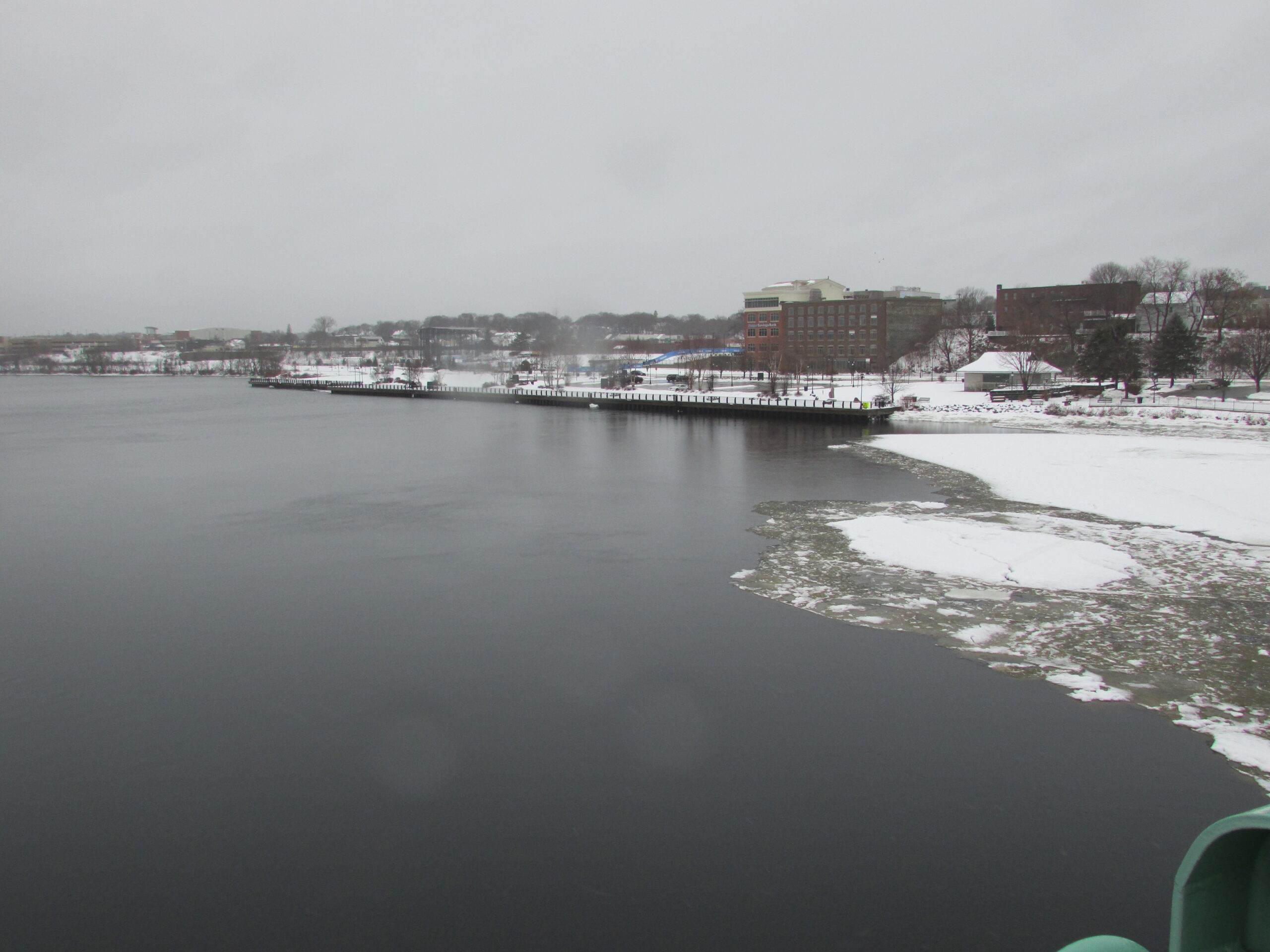 A peaceful view of the Penobscot River flowing past the snow covered Bangor waterfront in Maine during winter.