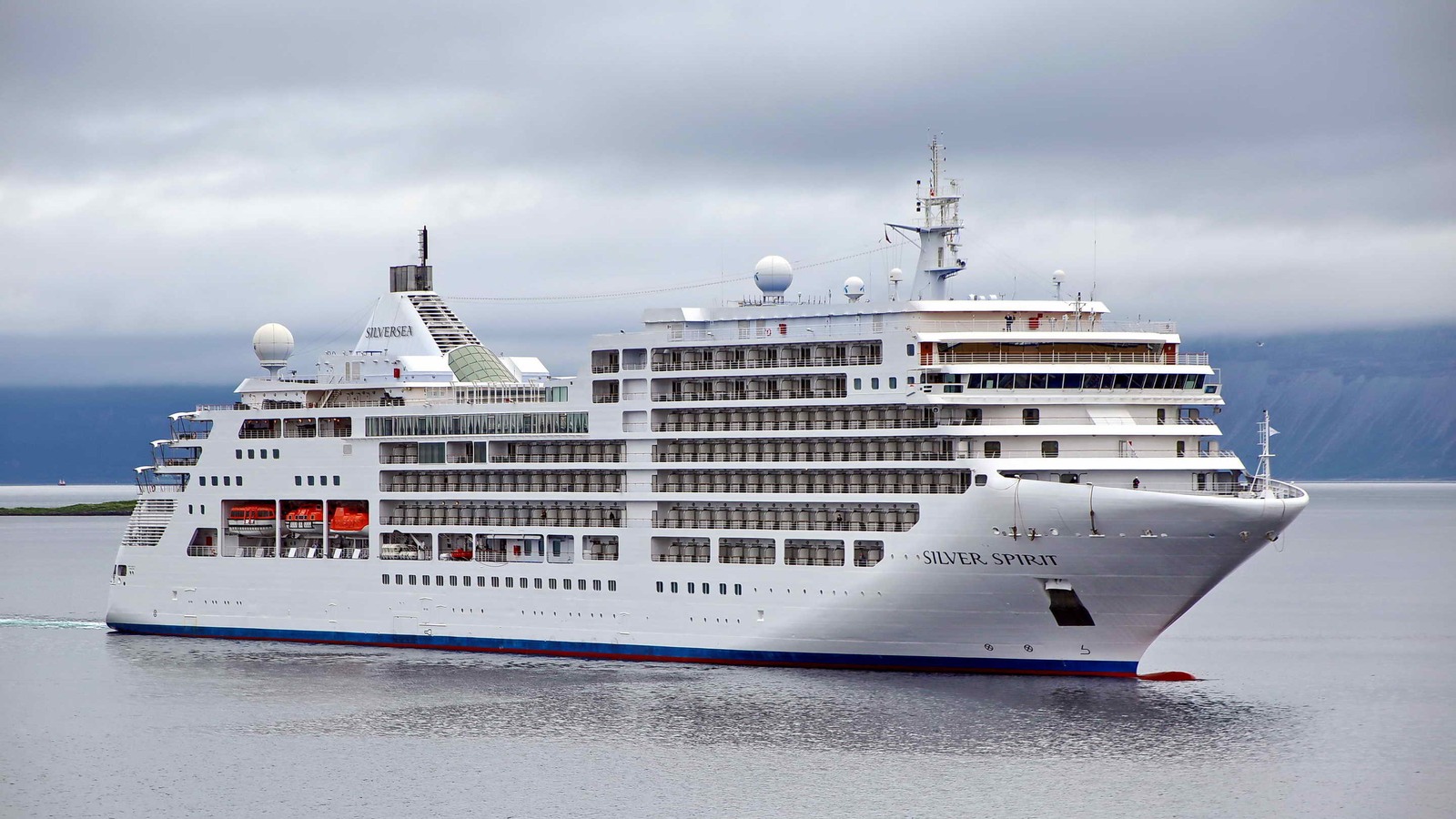 Silversea Silver Dawn cruise ship sailing past green coastal hills on a bright day