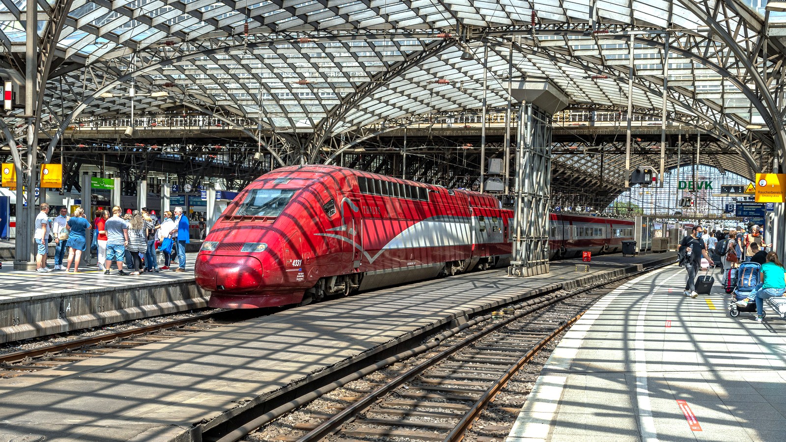 Red high-speed train standing at Cologne Hauptbahnhof platforms under a bright station roof
