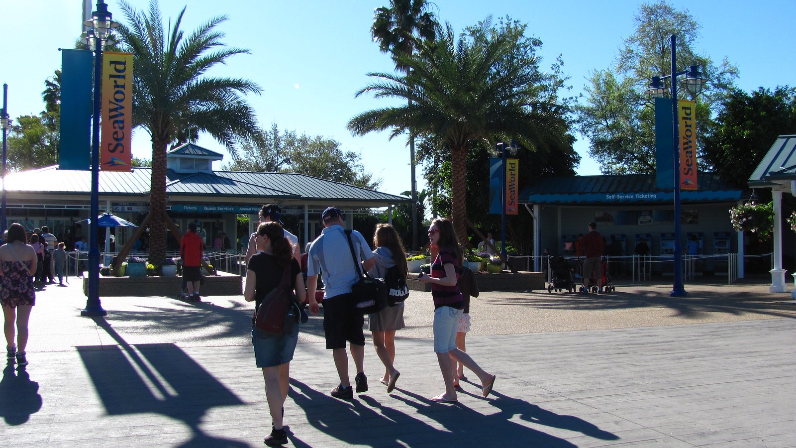 Guests walking through the SeaWorld Orlando entrance plaza toward ticket windows and self-service kiosks