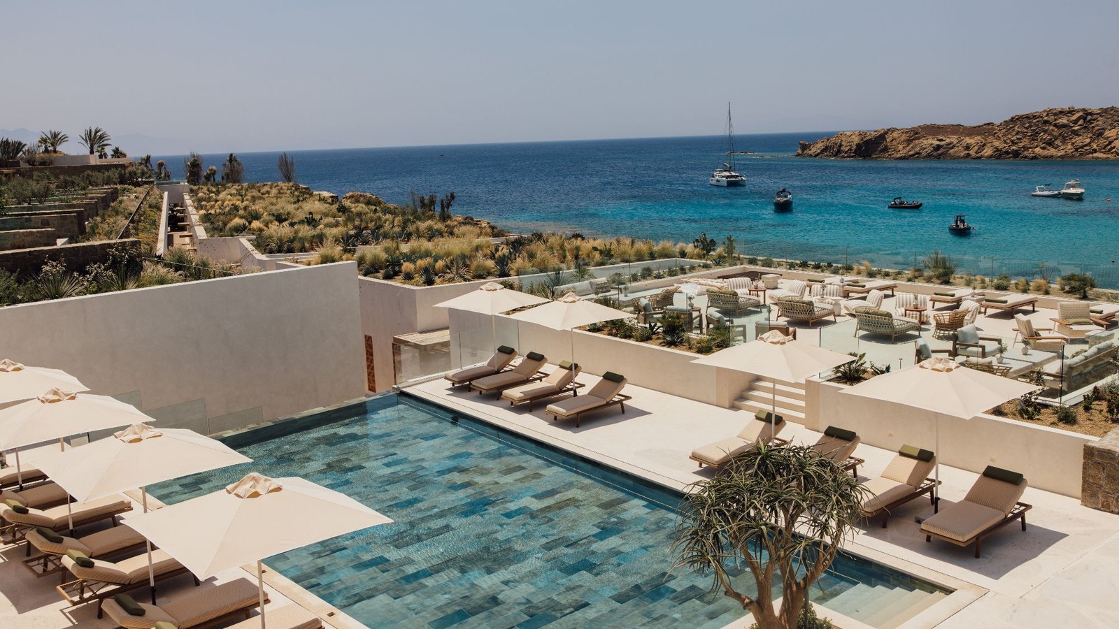 Infinity pool and lounge deck at Fouquet Mykonos overlooking turquoise Aegean waters and boats