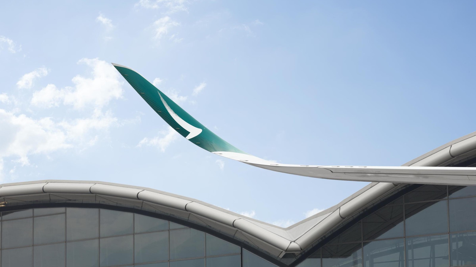 Cathay Pacific green brush-wing wingtip rising above an airport terminal roof