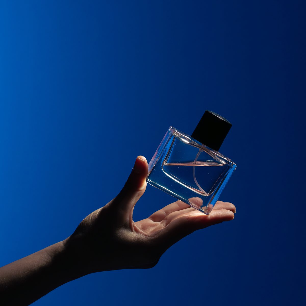 Glass perfume bottle held on an open hand against a blue background