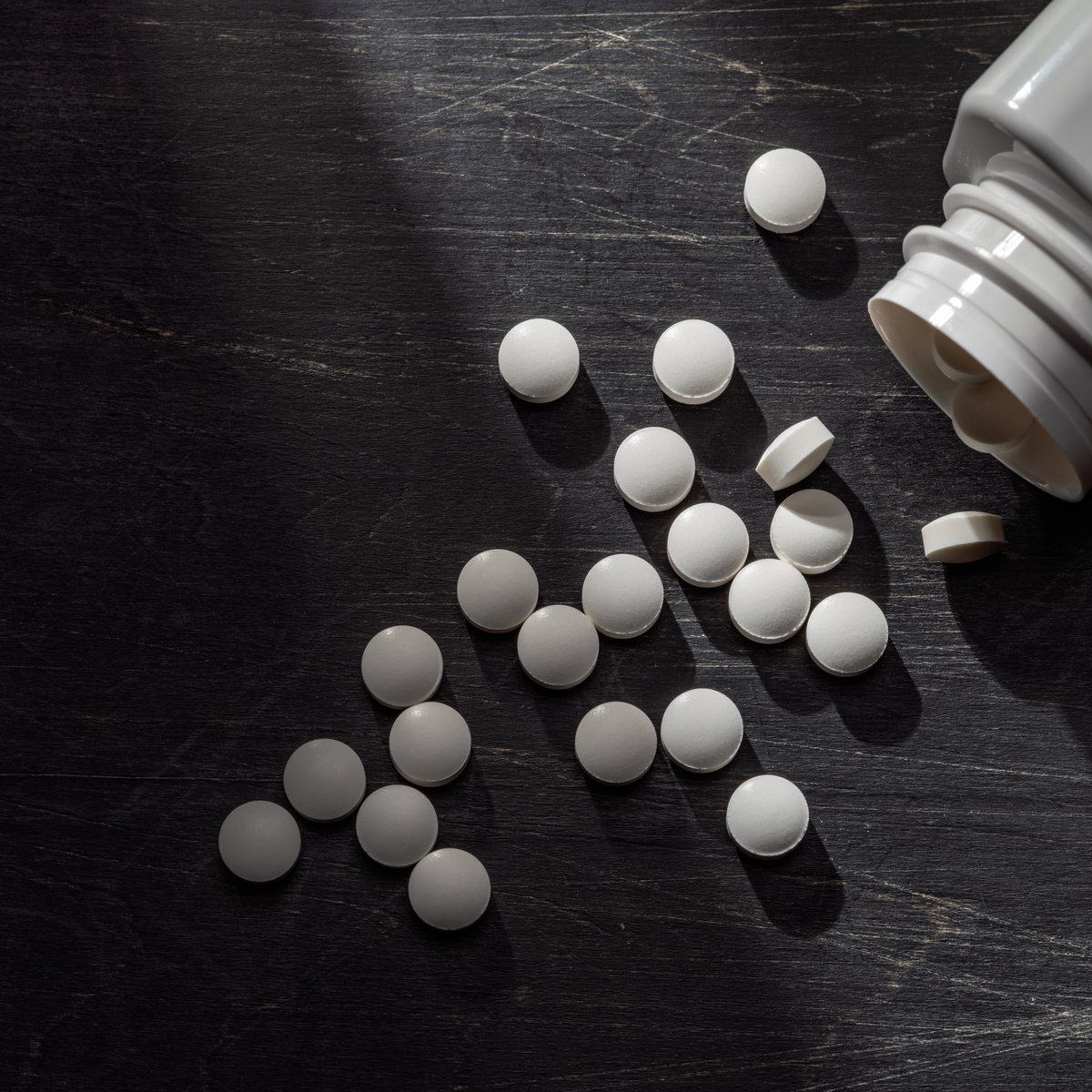 White vitamin tablets spilling from a bottle on a dark surface