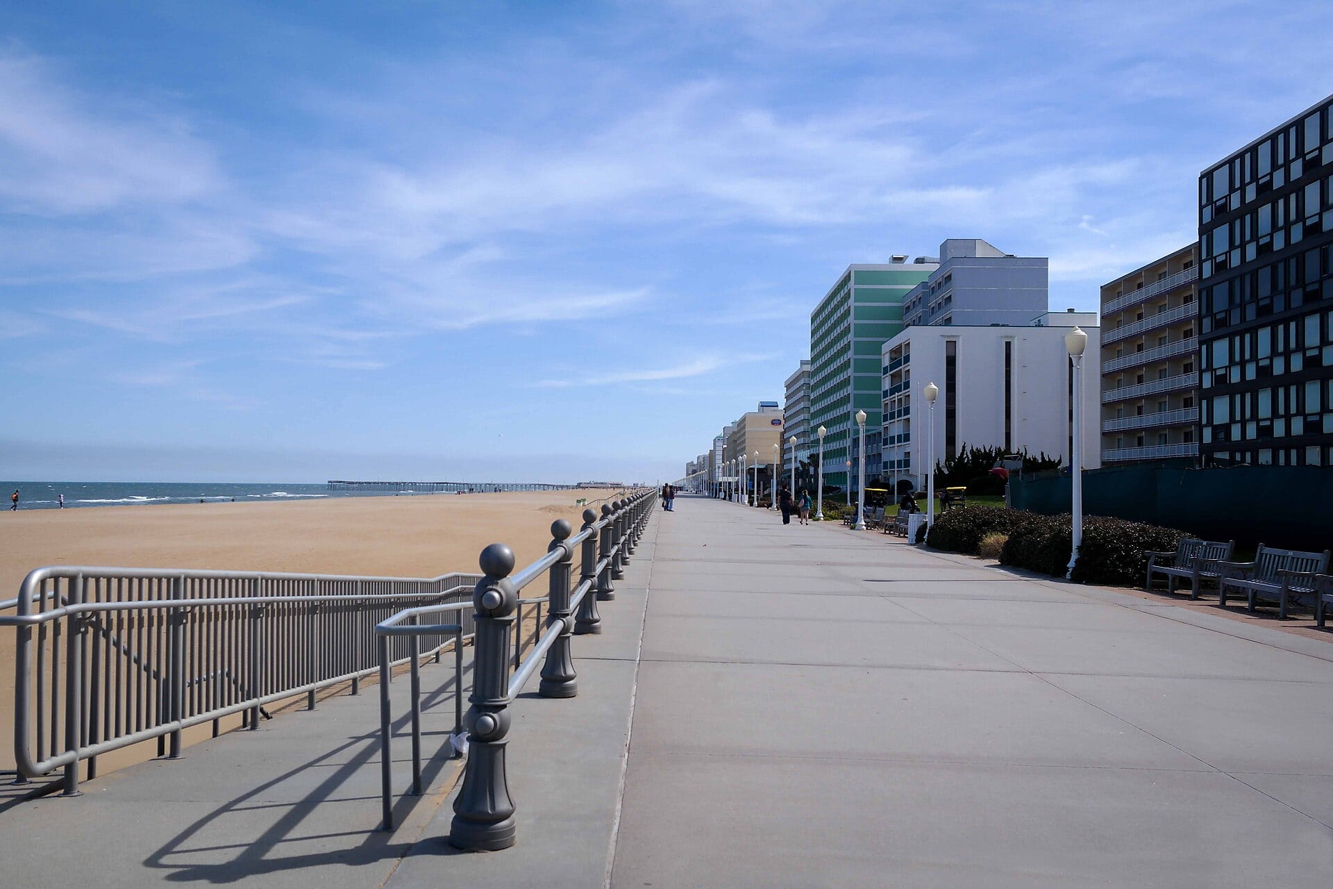 The bustling, wide sandy beach and adjacent oceanfront boardwalk in Virginia Beach under a bright sunny sky.