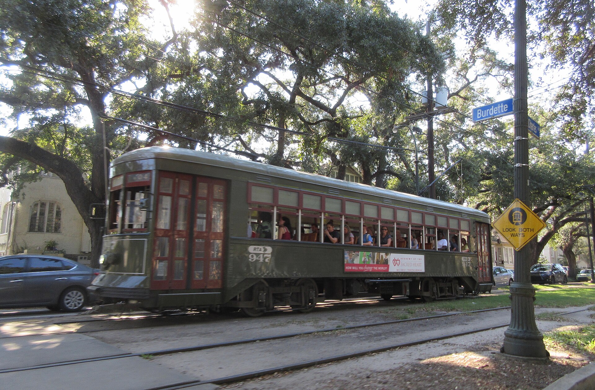 A green St. Charles Avenue streetcar passing under live oaks in New Orleans