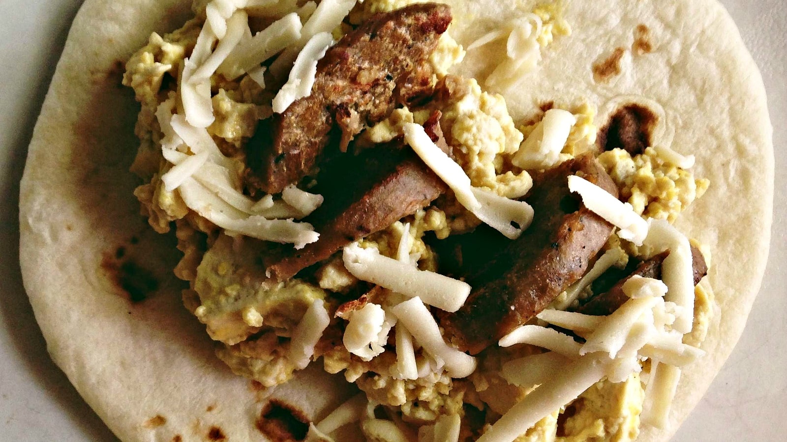 Vegan breakfast taco with egg-style filling, cheese, and sliced plant-based sausage
