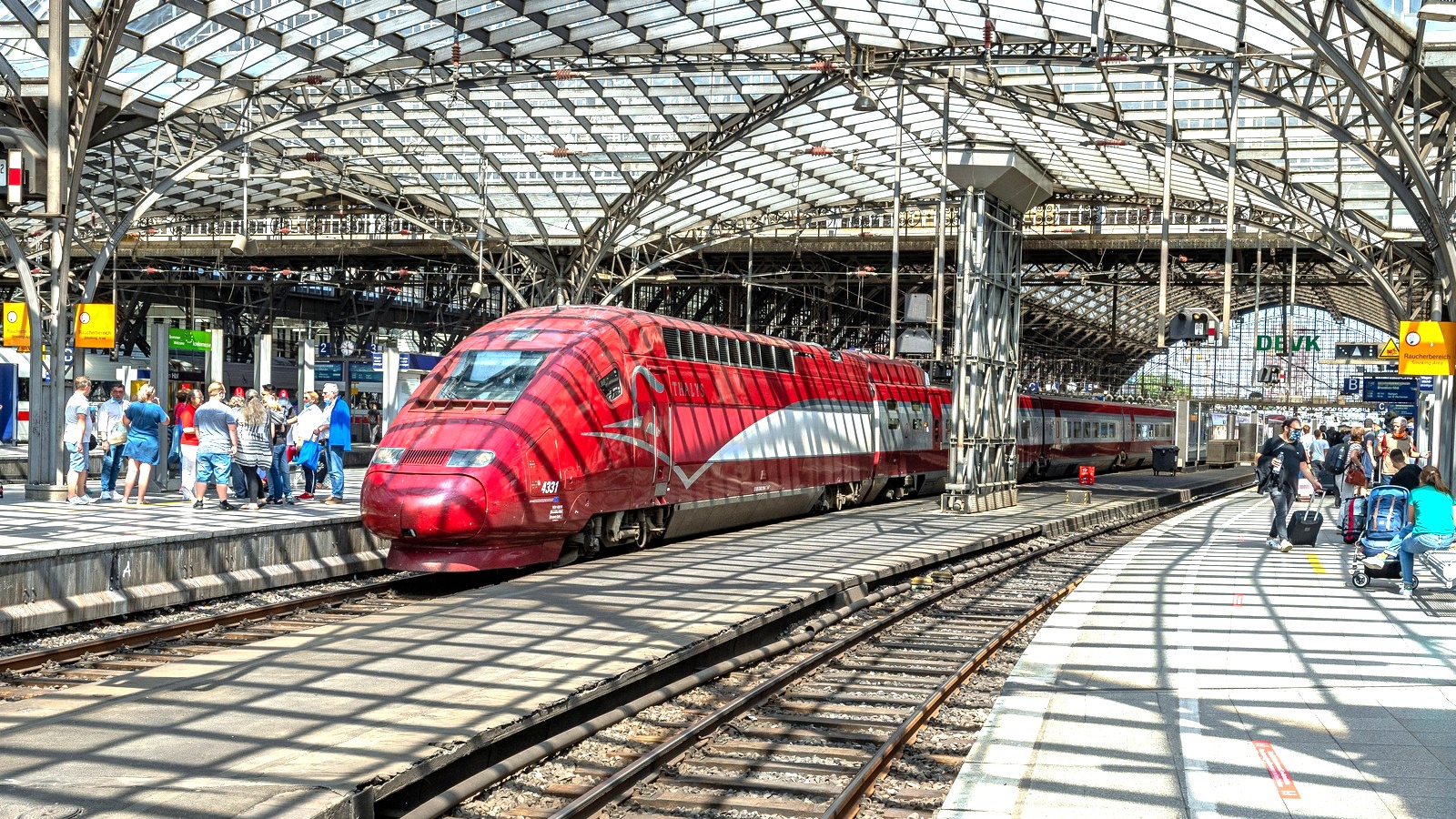 Red high-speed train standing at Cologne Hauptbahnhof platforms under a bright station roof