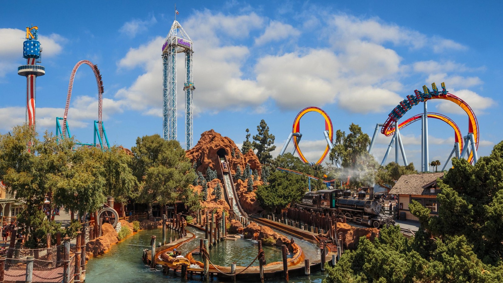 Daytime overview of Knott's Berry Farm with Calico River Rapids, Ghost Town train, and HangTime coaster under blue sky