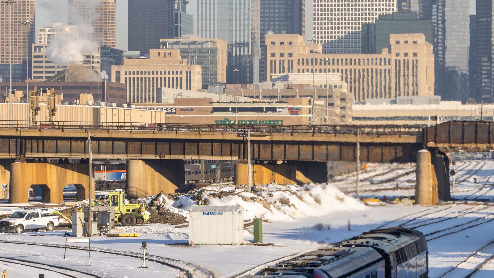 An Amtrak train moves through a snowy Chicago rail yard with the downtown skyline beyond