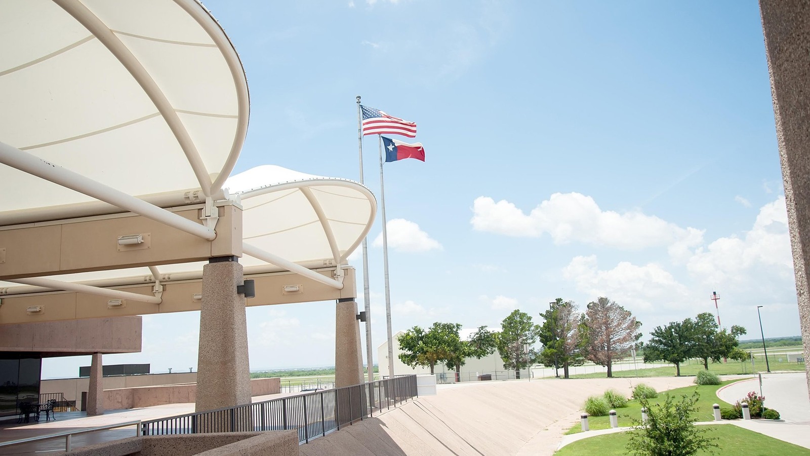 Daylight terminal canopy at Abilene Regional Airport with U.S. and Texas flags over the airport roadway