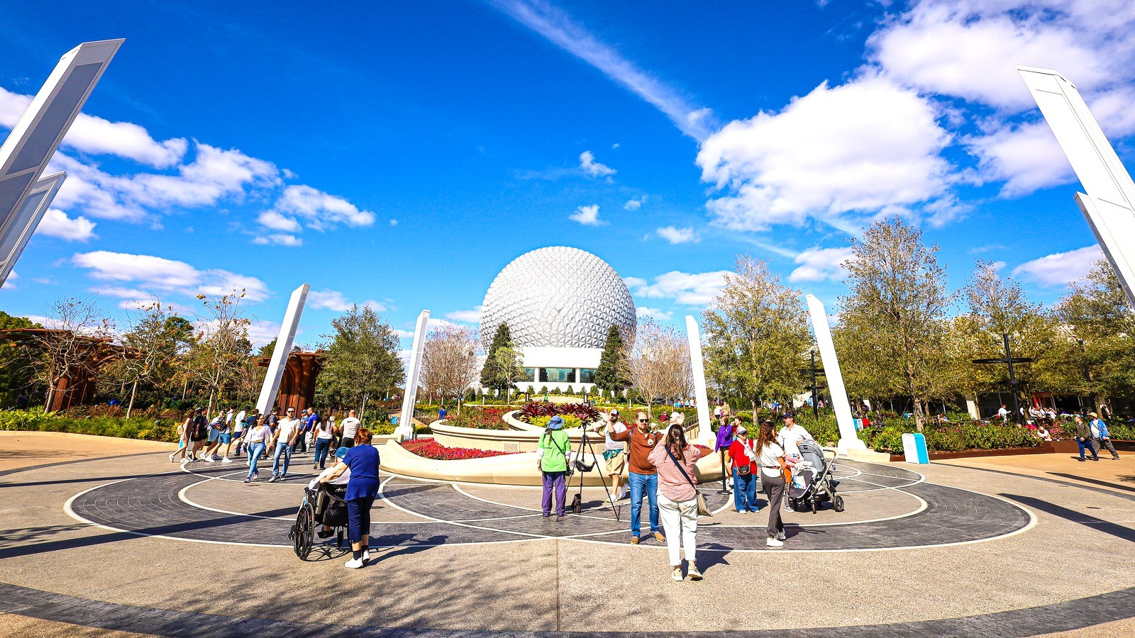 Daytime view of EPCOT World Celebration Gardens with landscaped planters and Spaceship Earth in the background