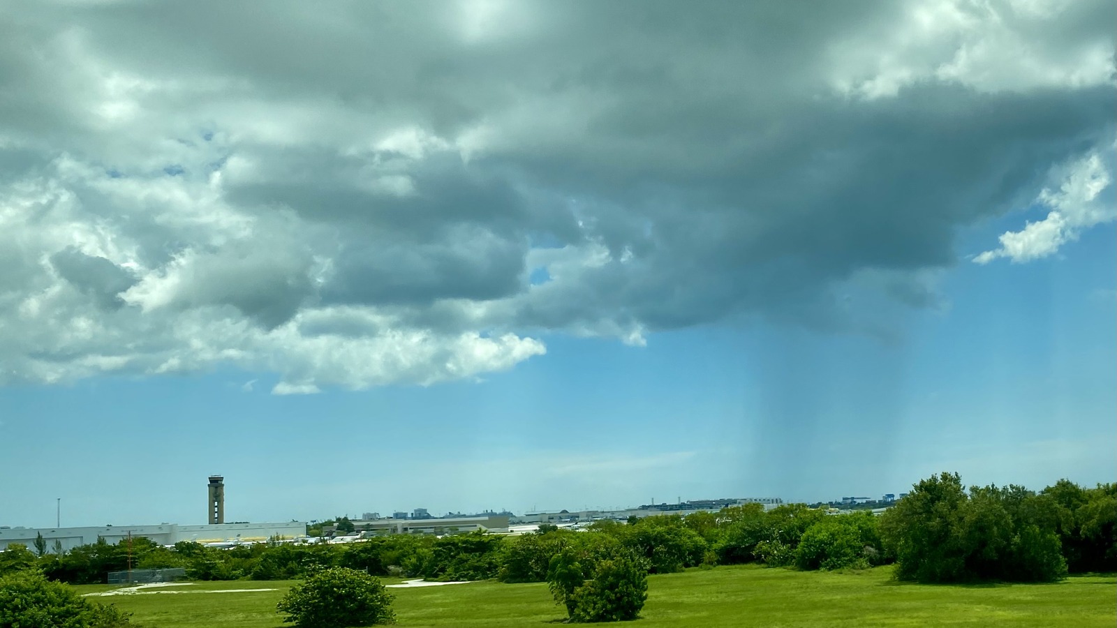 Fort Lauderdale-Hollywood International Airport terminal complex and control tower across open field under partly cloudy sky