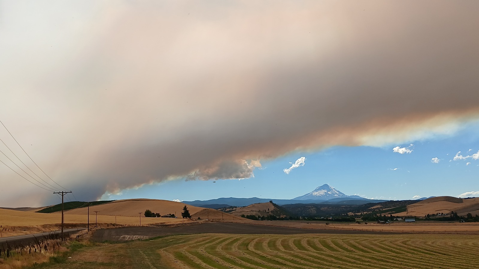 Wildfire smoke plume over dry hills with Mount Hood visible to the north