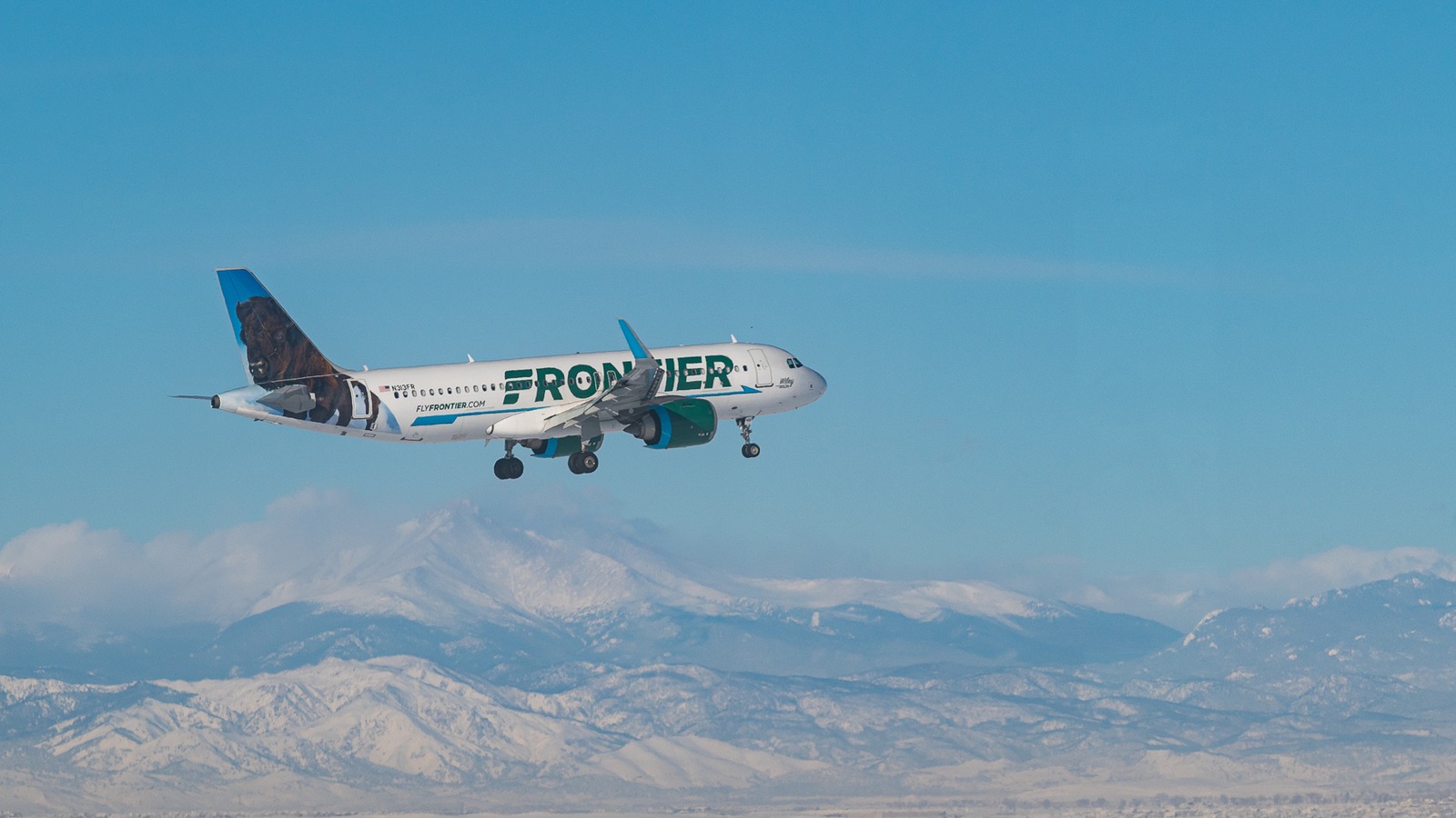 Frontier Airlines jet on approach at Denver International Airport with Rocky Mountains behind