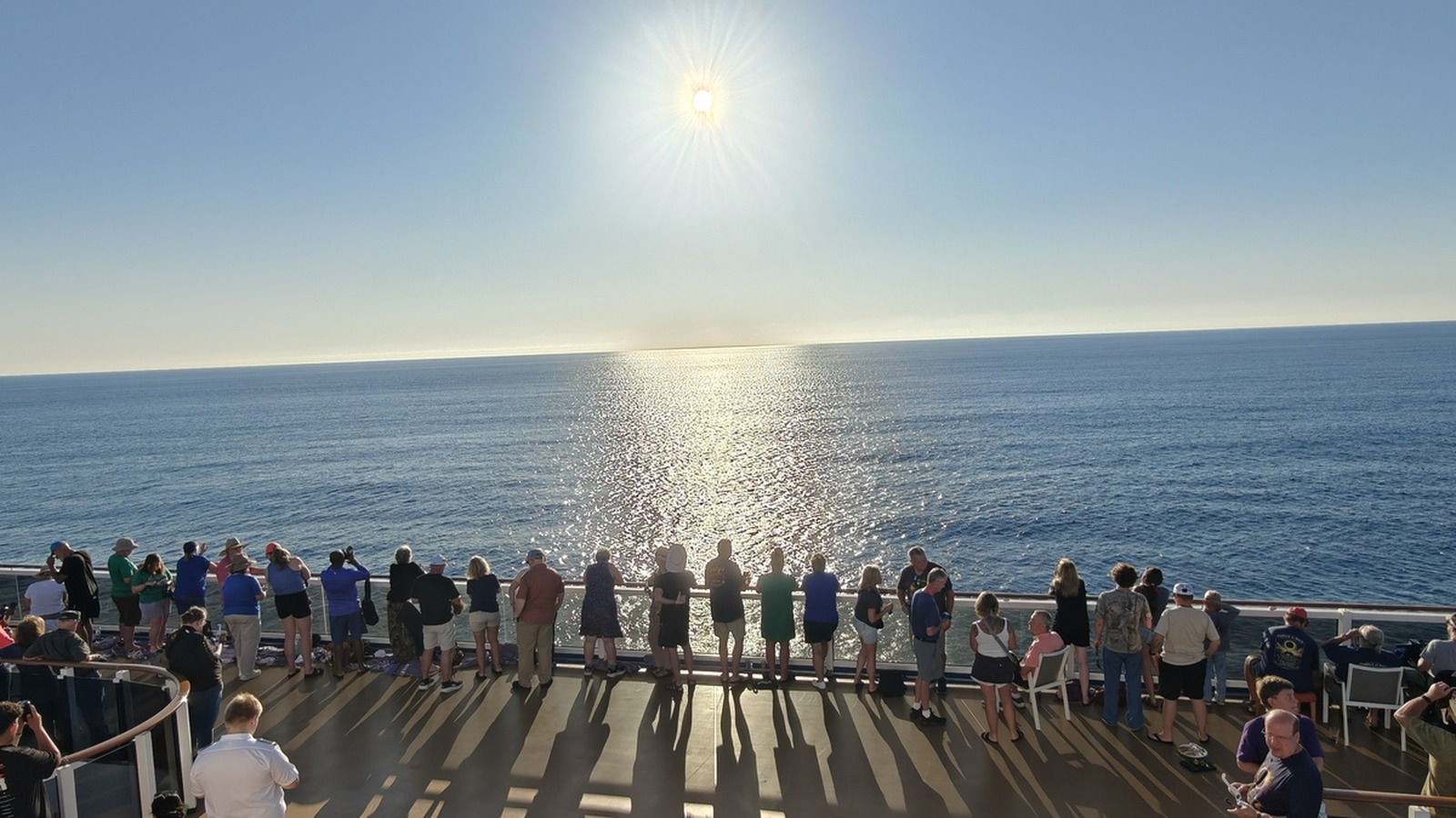 Guests along the rail of Carnival Legend watching the sun over open water during the official first eclipse sailing