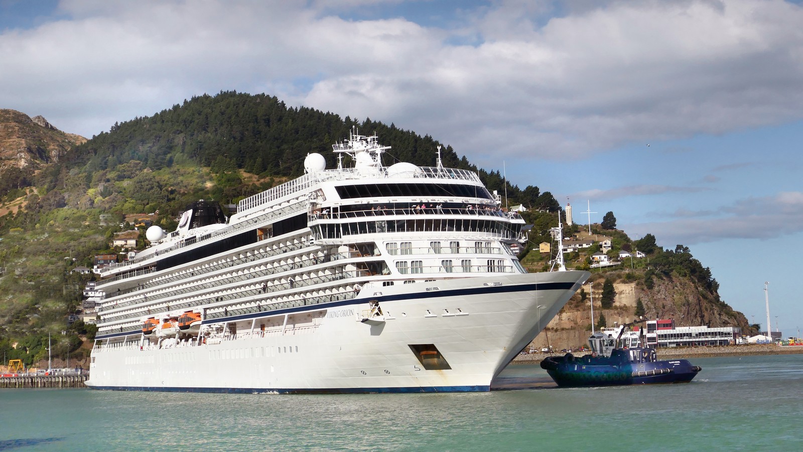 Viking Orion ocean cruise ship at a green hillside port with a tug nearby