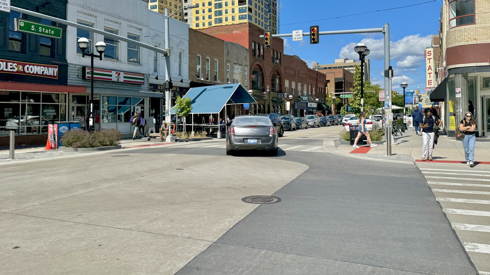Brick storefronts along State Street in downtown Ann Arbor with people on the pavement and a blue sky above