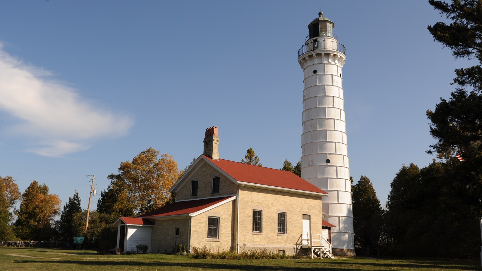 The white tower of Cana Island Lighthouse beside its stone keeper's house with a red roof, on green grass under a blue sky
