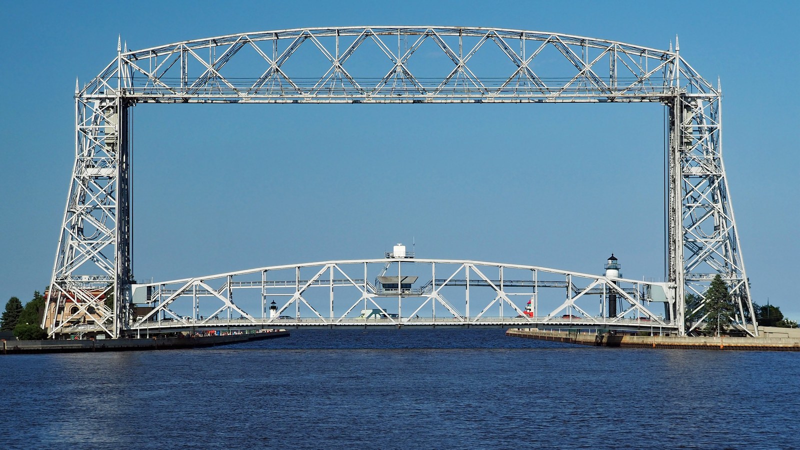 The steel Aerial Lift Bridge spanning the Duluth ship canal under a clear blue sky, with the pier lighthouses either side
