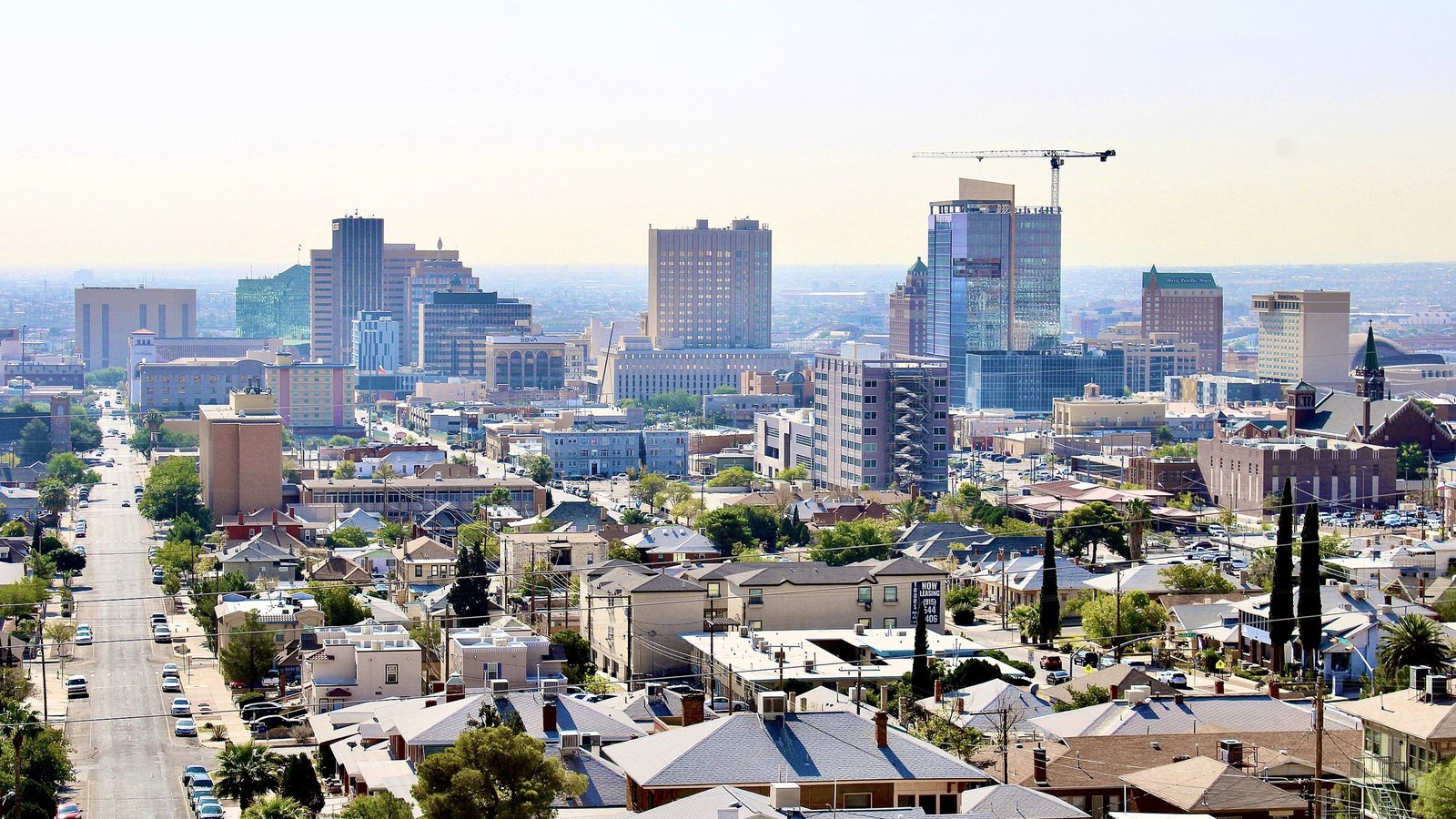 The downtown El Paso skyline seen over the rooftops of a hillside neighborhood, with a long straight street running down toward the towers
