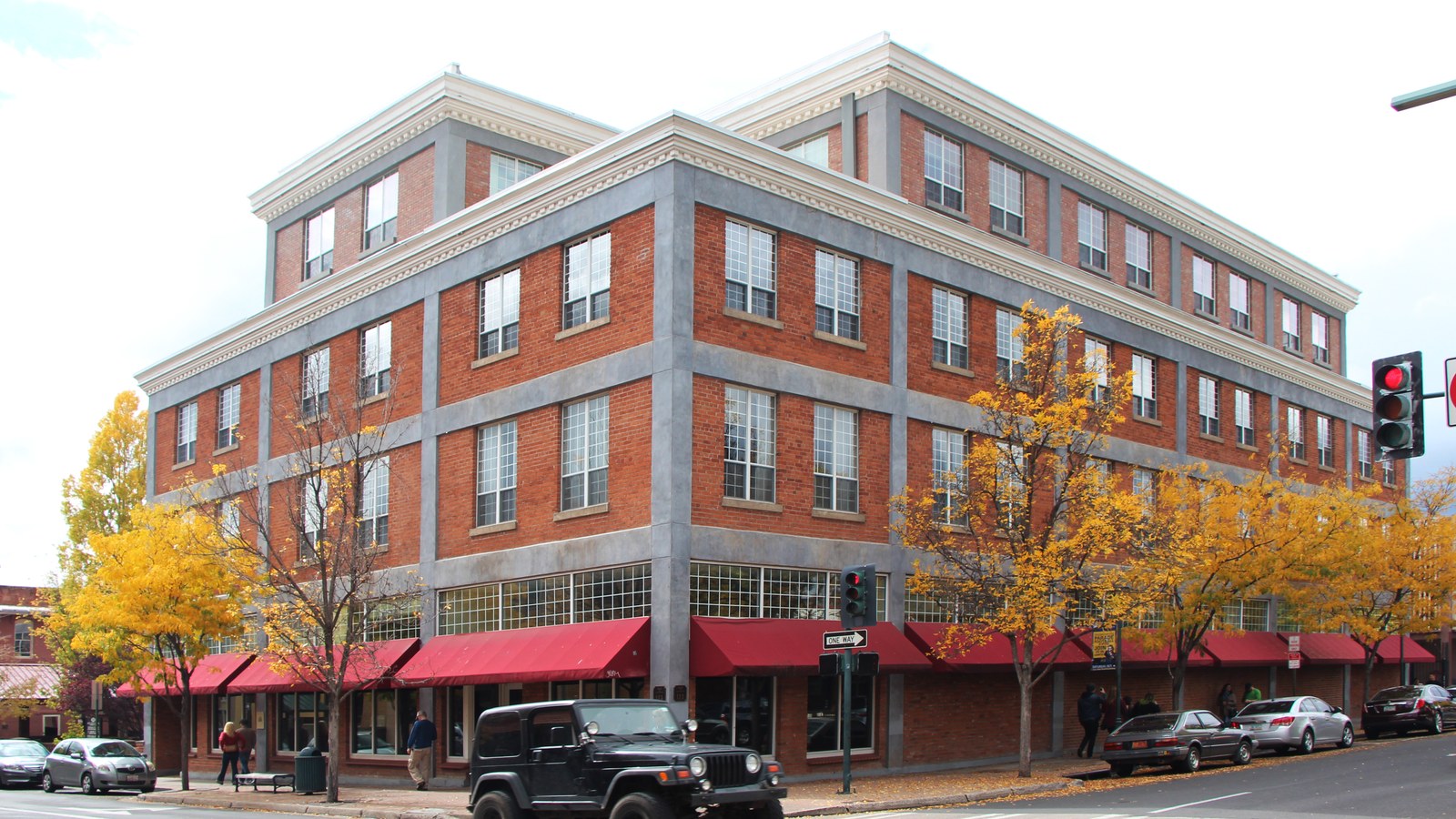 The red brick Babbitt Building on a corner in historic downtown Flagstaff, Arizona, with fall foliage and parked cars along the street