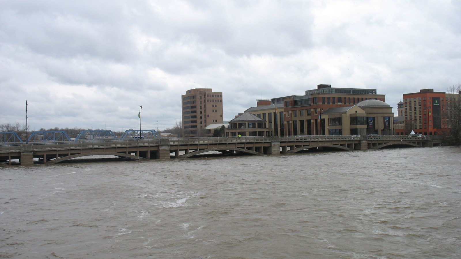 The Grand Rapids Public Museum building on the Grand River bank seen along the Pearl Street bridge under an overcast sky