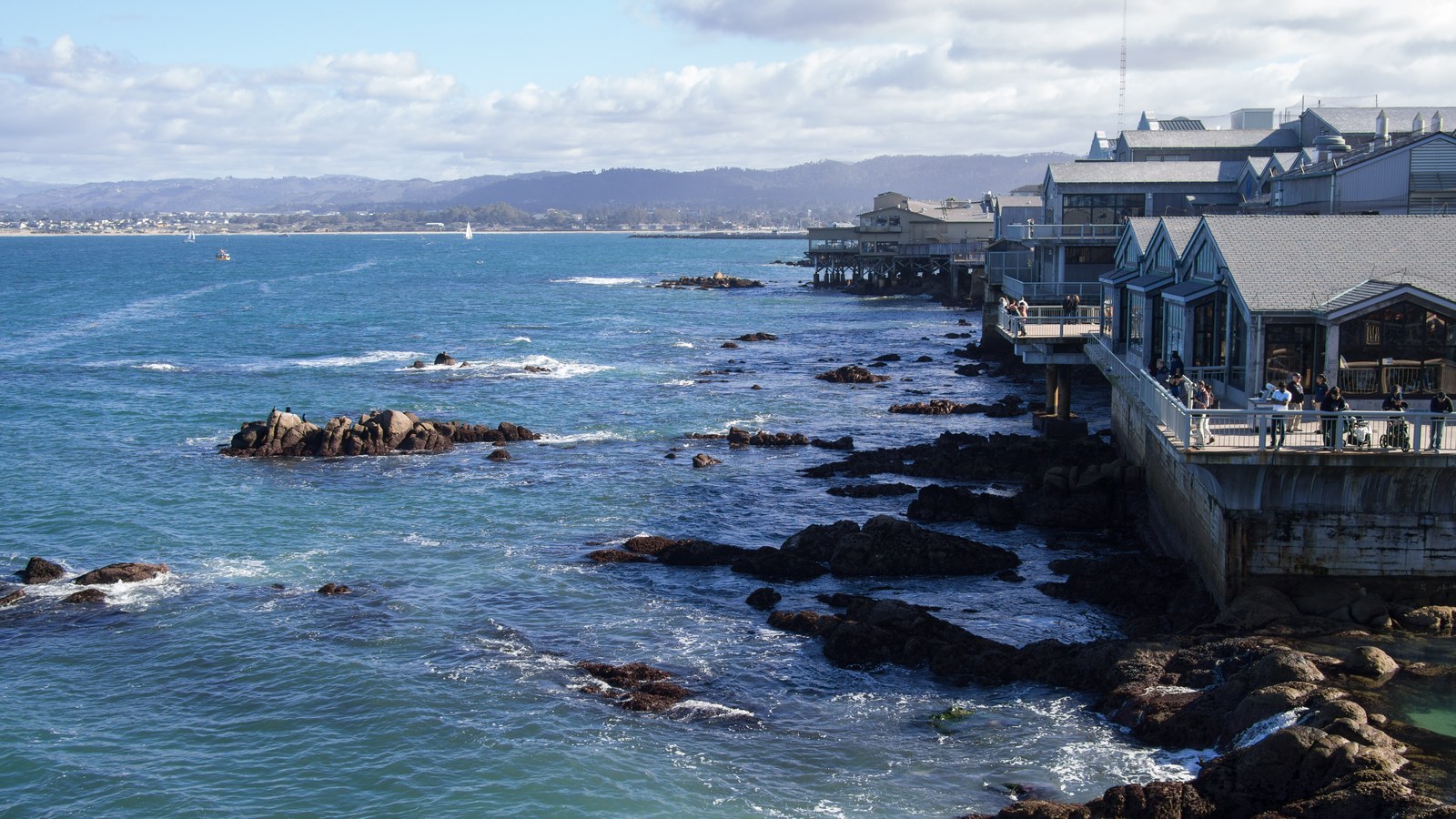 Rocky shoreline and blue water of Monterey Bay with the buildings of Cannery Row along the waterfront