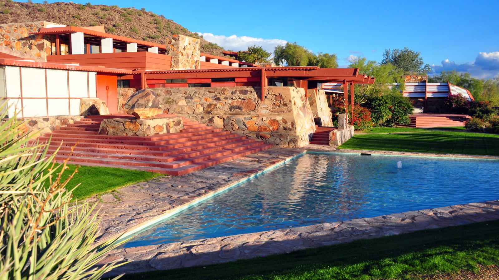The red beams and desert masonry terraces of Taliesin West in Scottsdale, Arizona beside its pool under a blue sky