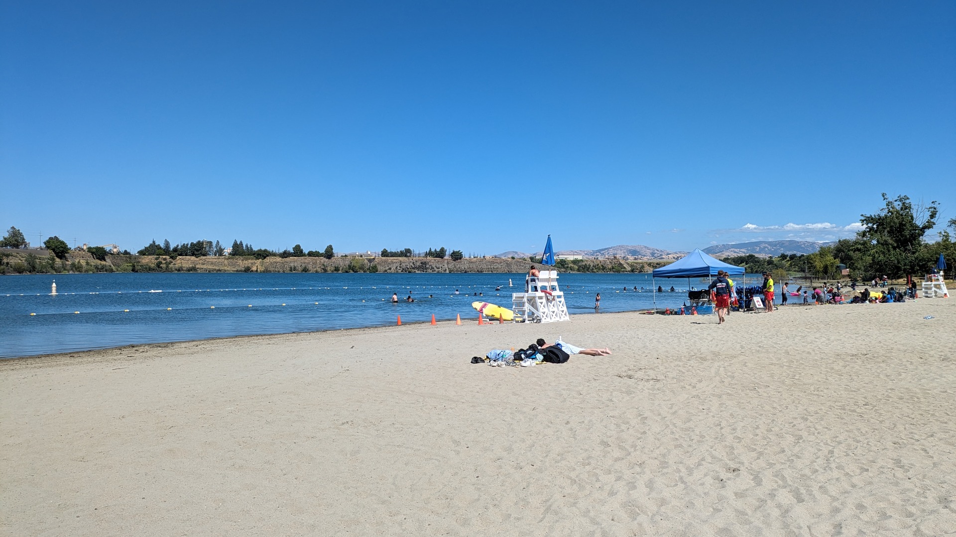 Swimmers, a lifeguard stand and sunbathers on the sand beach at Shadow Cliffs Regional Recreation Area in Pleasanton, California