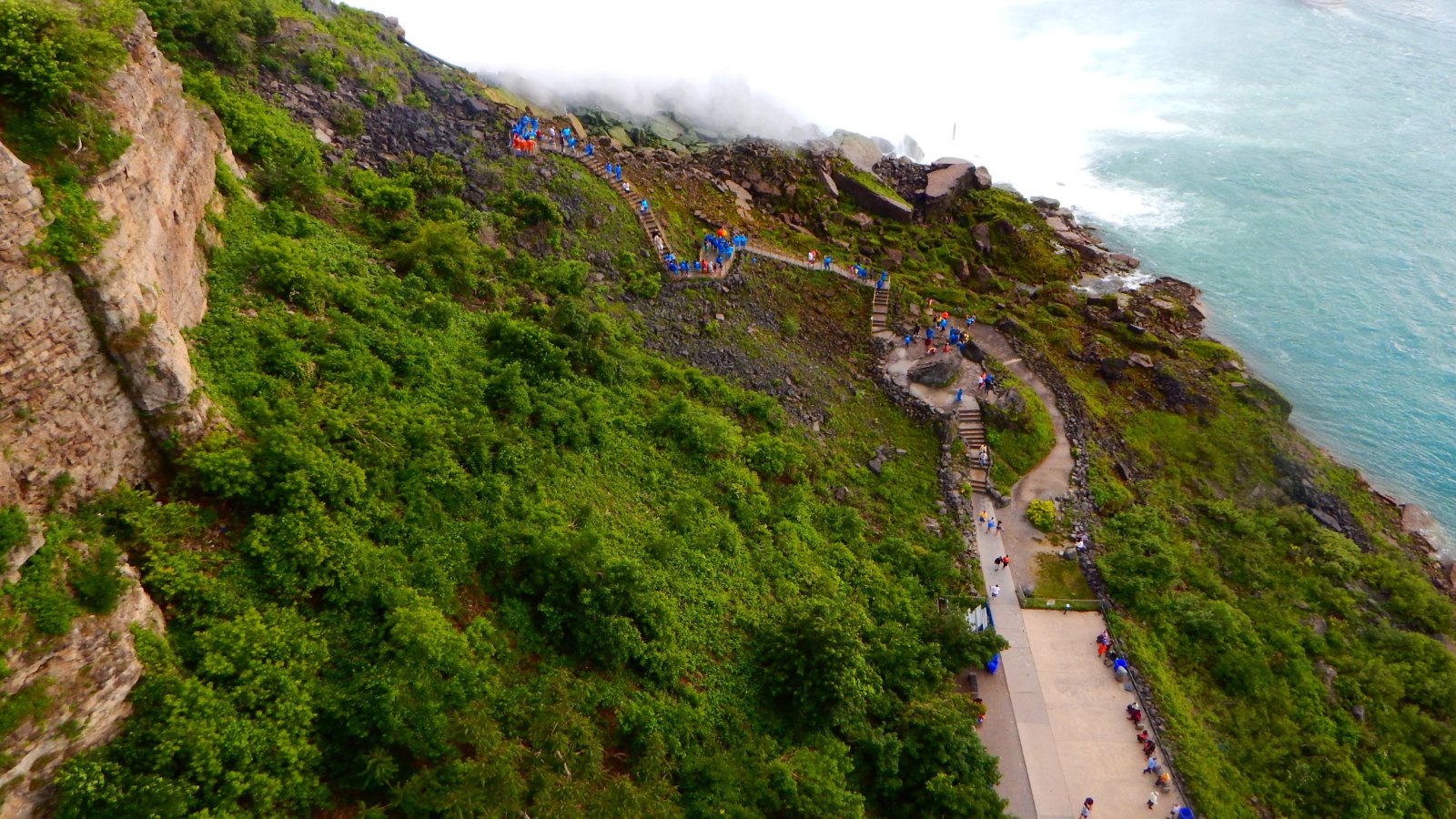 Elevated view of the Niagara Falls State Park cliffside walkway with falls mist and a tour boat below