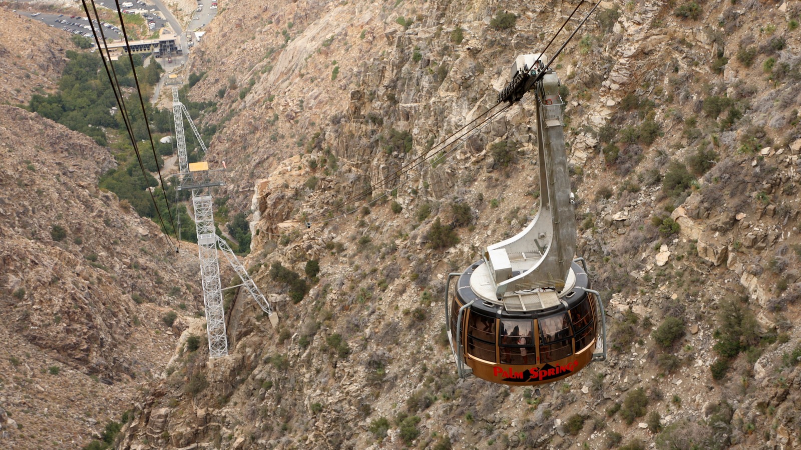 A red and white Palm Springs Aerial Tramway cable car climbing the rocky wall of Chino Canyon above Palm Springs, California