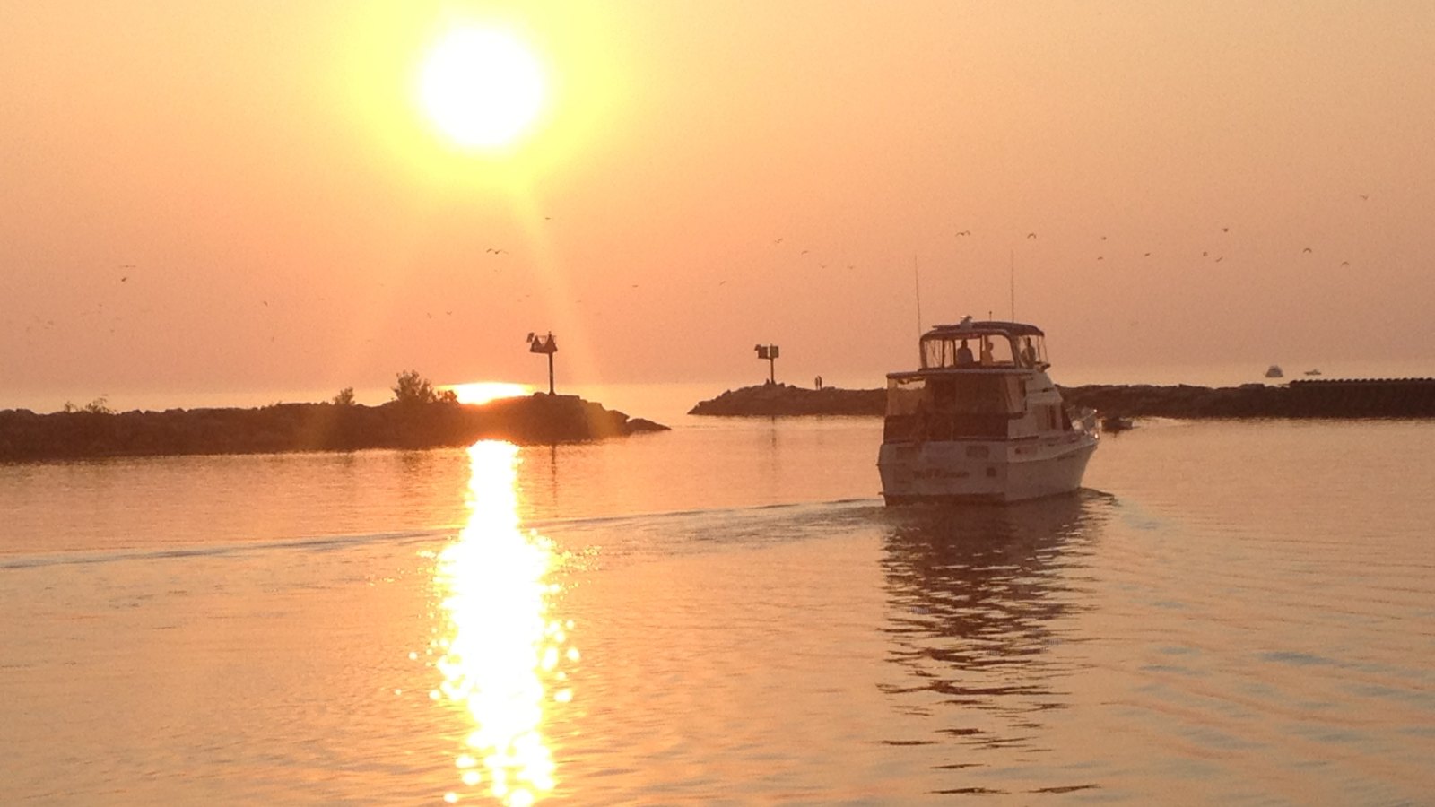 The New Buffalo harbor breakwater entrance at sunset on Lake Michigan with a cabin cruiser returning