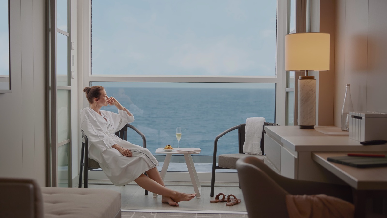 A traveler in a robe relaxing inside a Celebrity Xcel Infinite Veranda stateroom