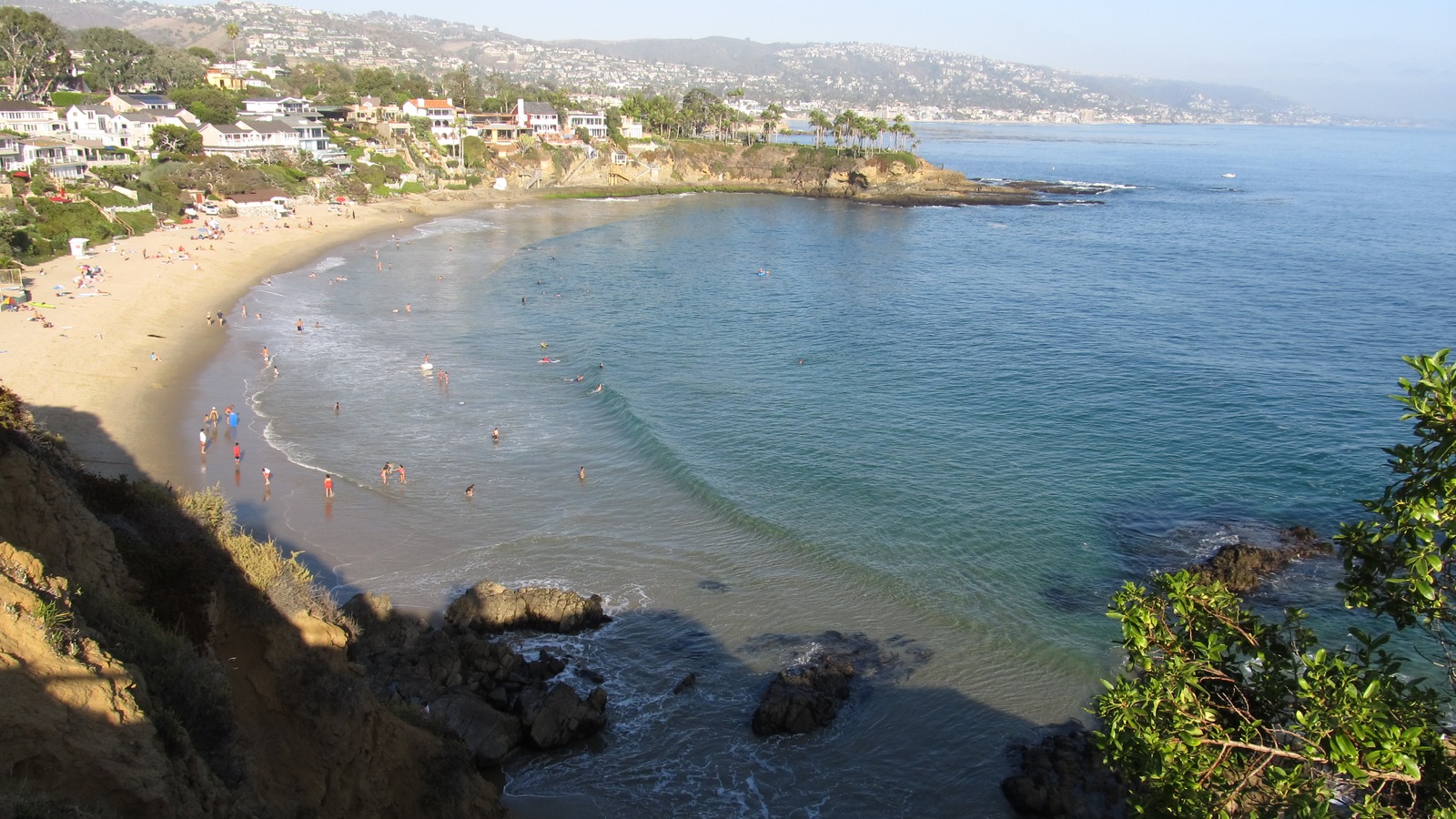 Cliff-top view of Crescent Bay Point Park in Laguna Beach, California, with sandstone cliffs above a cove and houses along the shore