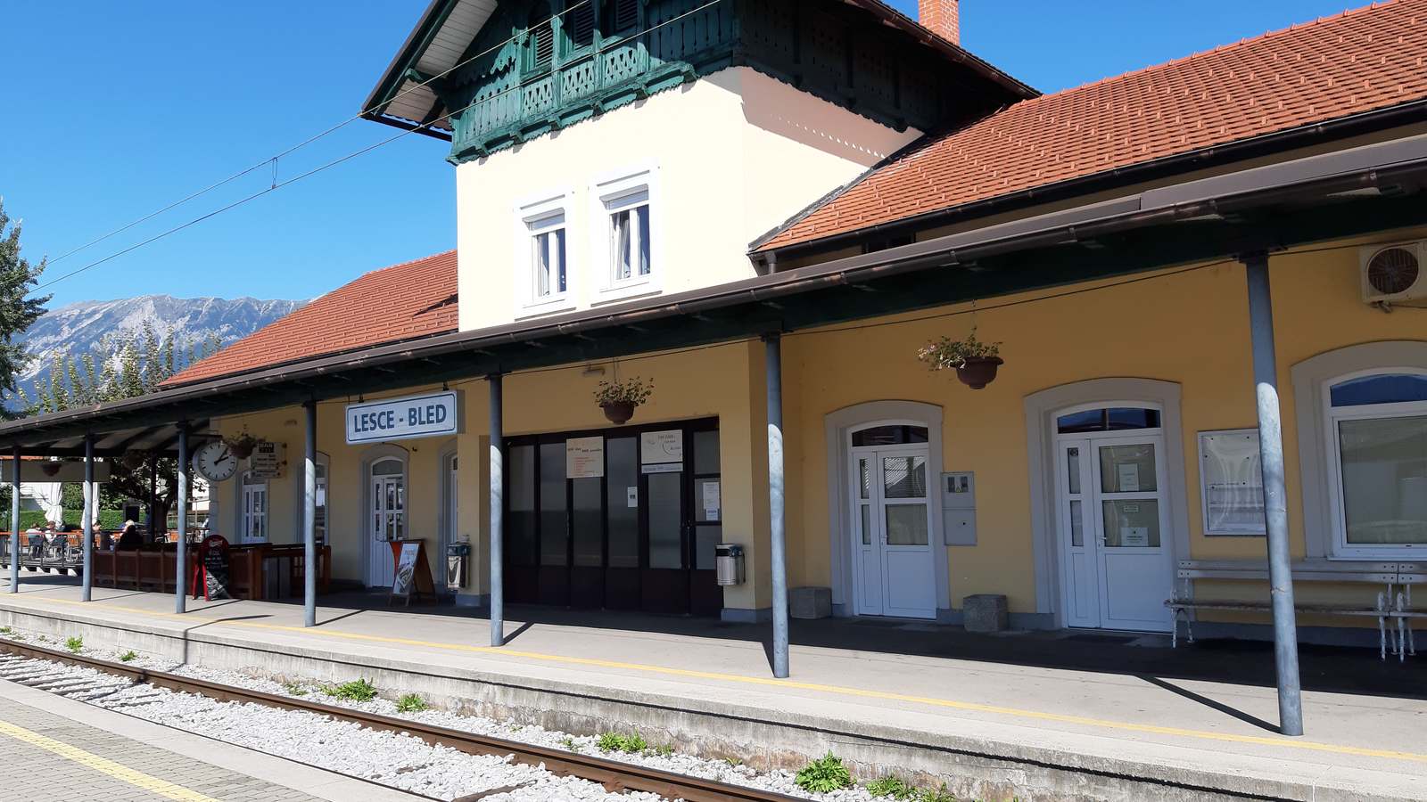 Lesce-Bled railway station building and platform under a blue sky with mountains behind