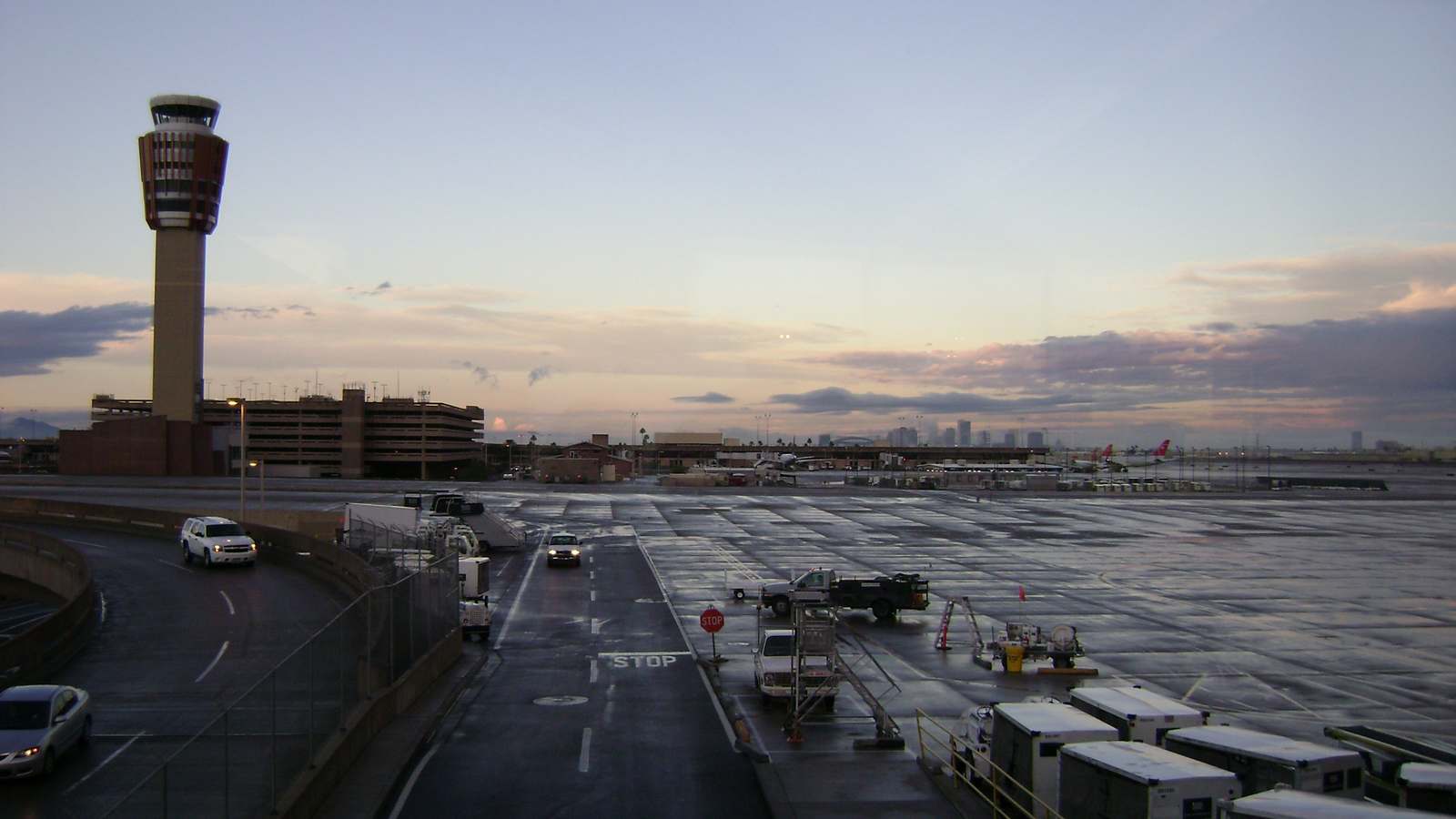 The Phoenix Sky Harbor air traffic control tower and a parking garage beside a wet airport ramp at dusk, with the downtown Phoenix skyline in the distance.