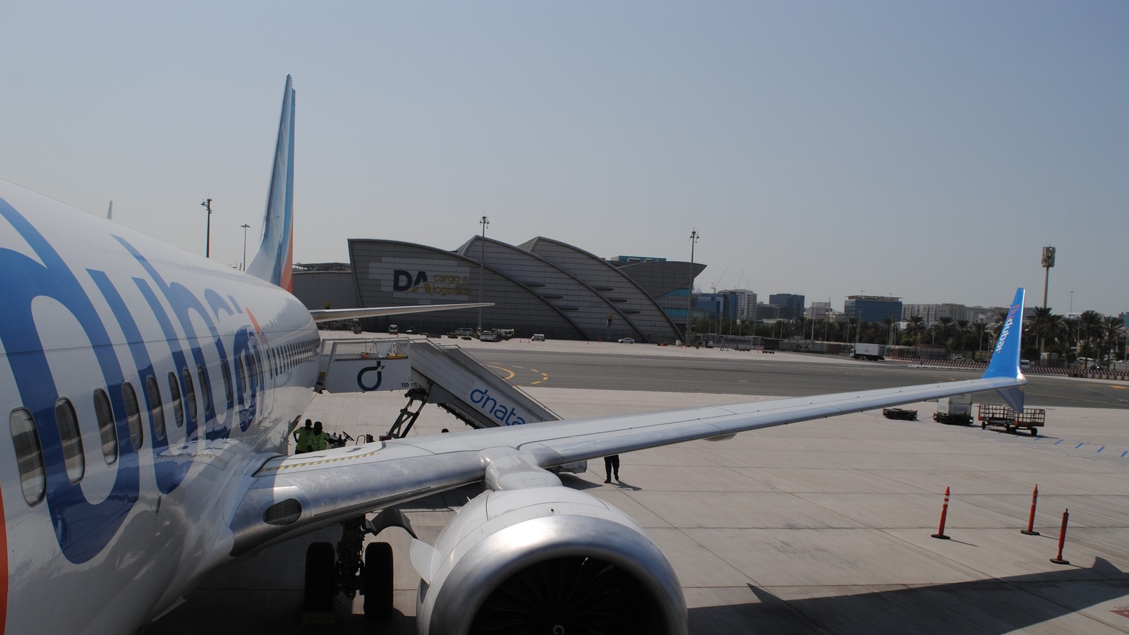 A flydubai jet parked at Dubai International Airport beside the DA cargo building and a dnata jet bridge, photographed in October 2024.