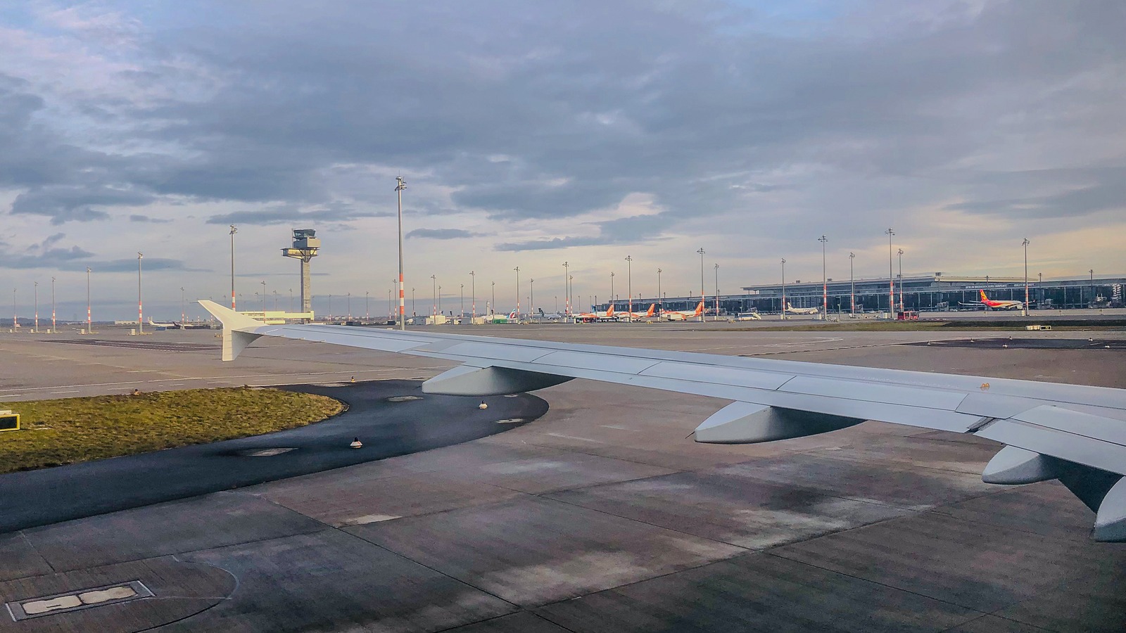 Daylight view over an aircraft wing across the apron at Berlin Brandenburg Airport with the control tower and Terminal 1 in the distance