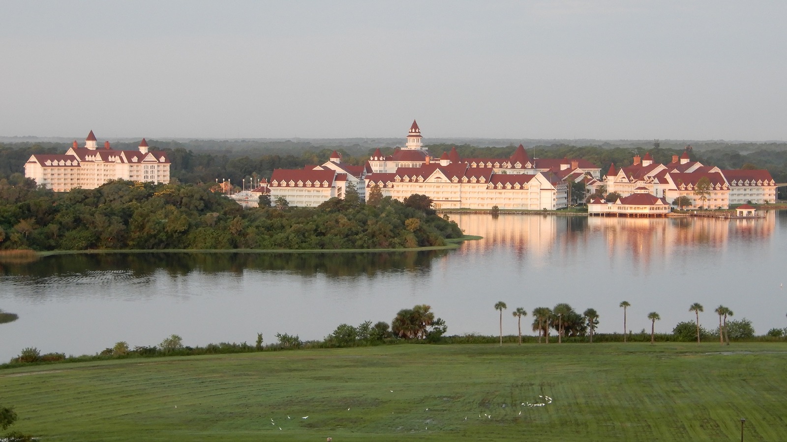 Disney's Grand Floridian Resort white Victorian buildings and red roofs across Seven Seas Lagoon at sunrise, photographed from Disney's Contemporary Resort