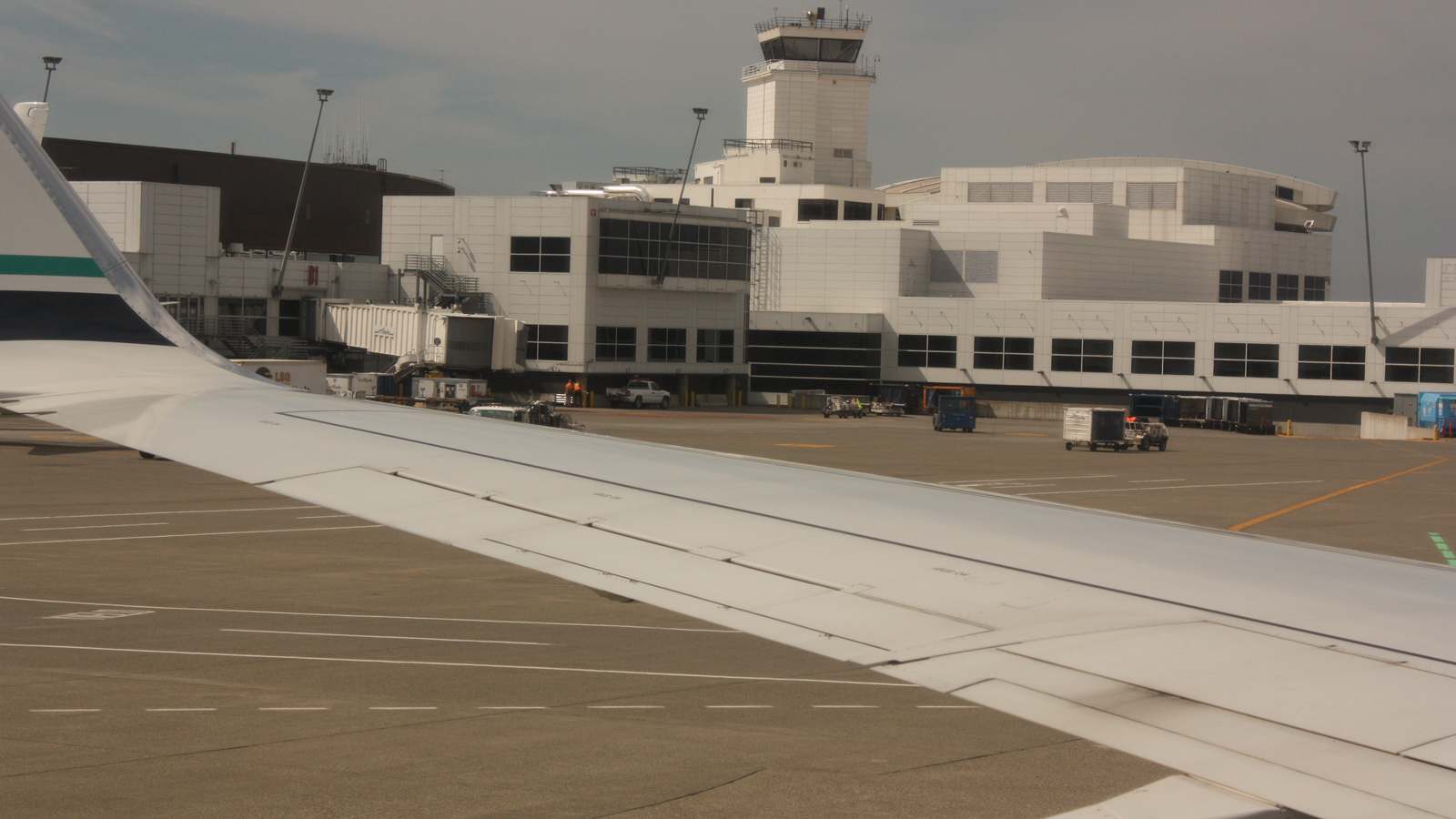 Seattle-Tacoma International Airport terminal buildings and control tower seen from an aircraft window with the wing in the foreground.